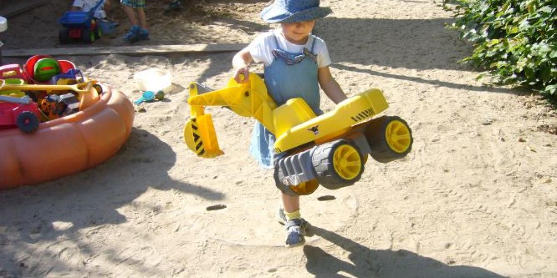 Kind mit Bagger im Sandkasten